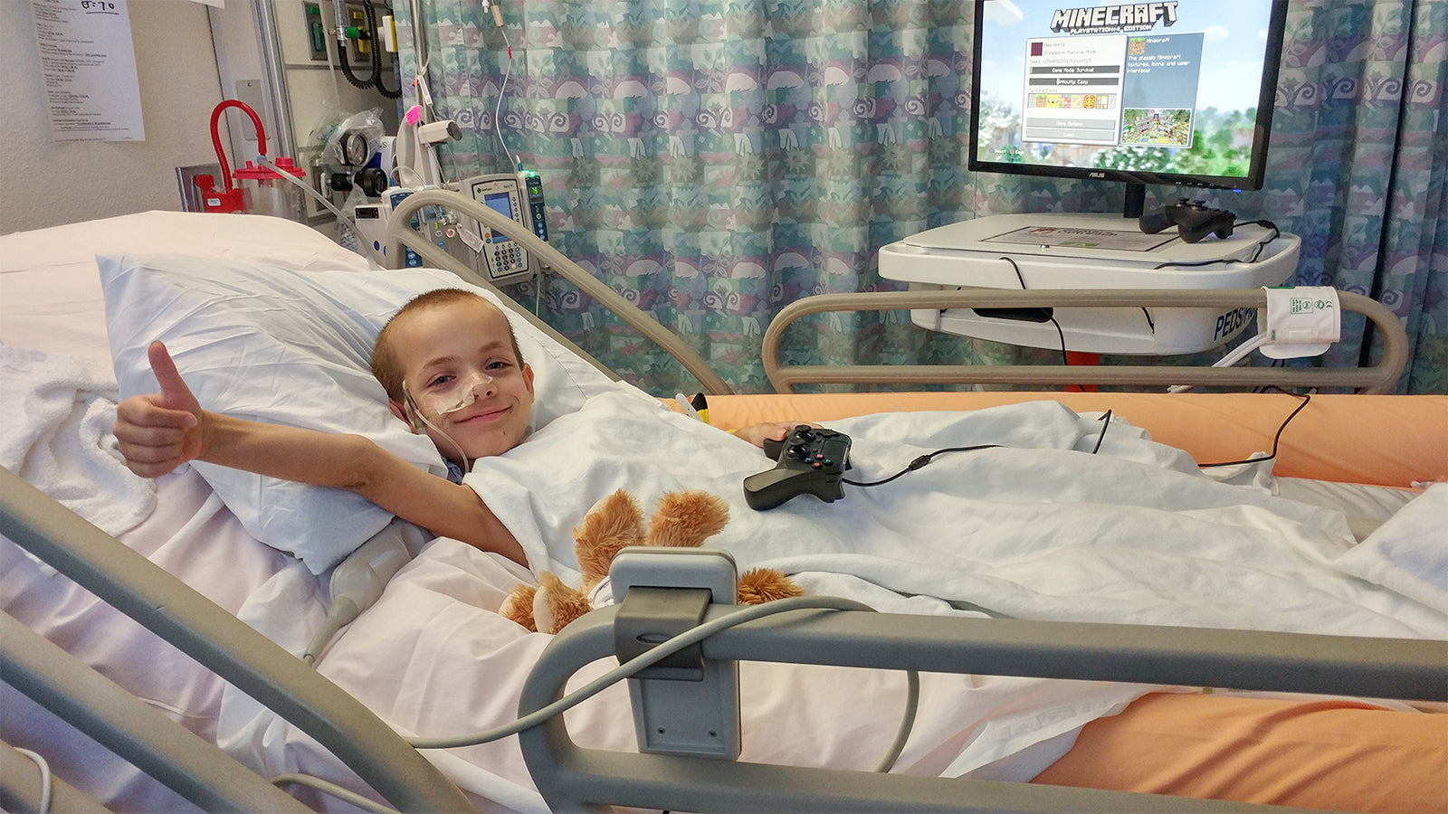 A child in care at a hospital, smiling and giving a thumbs up while playing video games