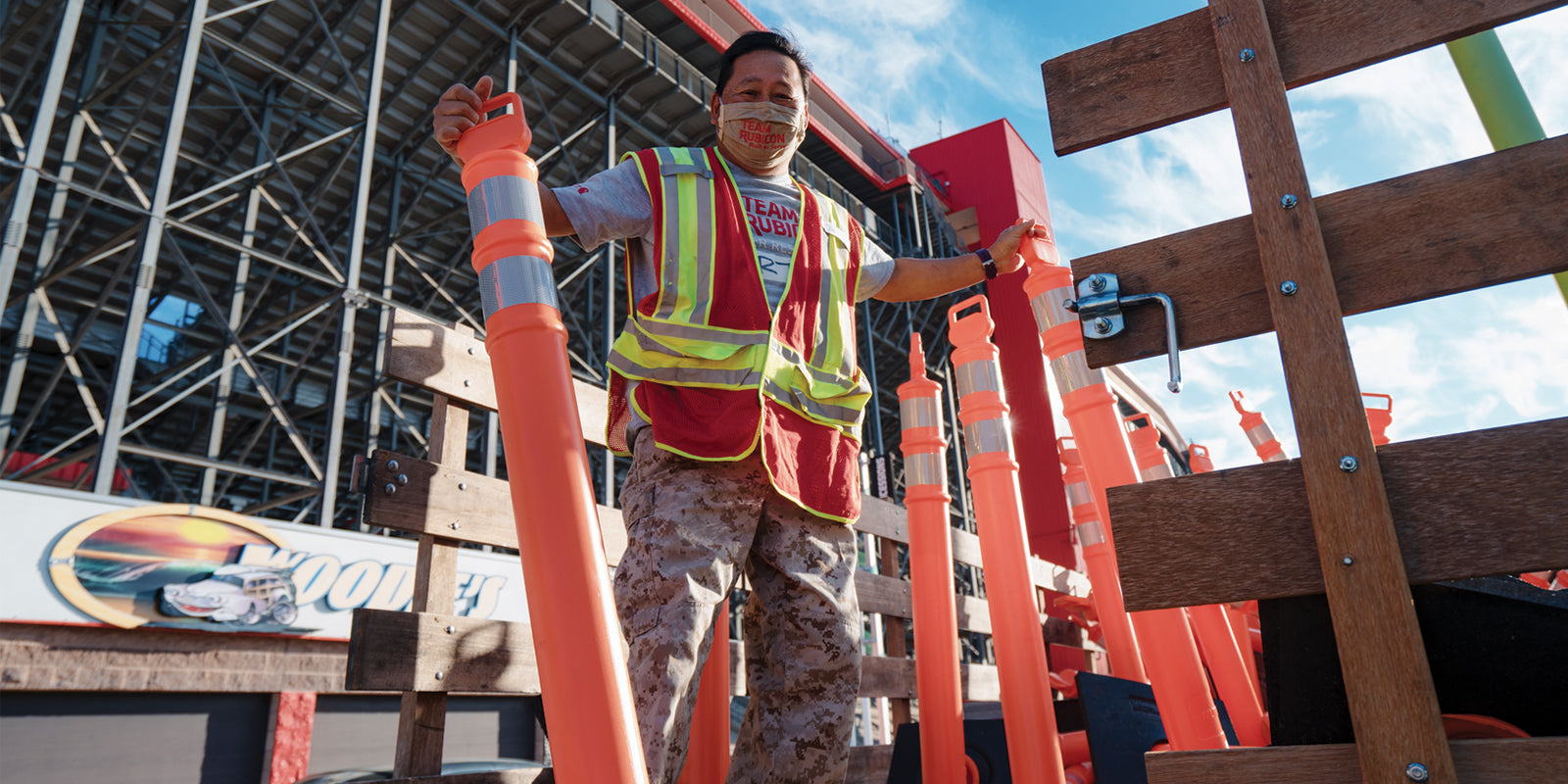 A Team Rubicon volunteer in a construction vest and mask stands holding traffic cones.