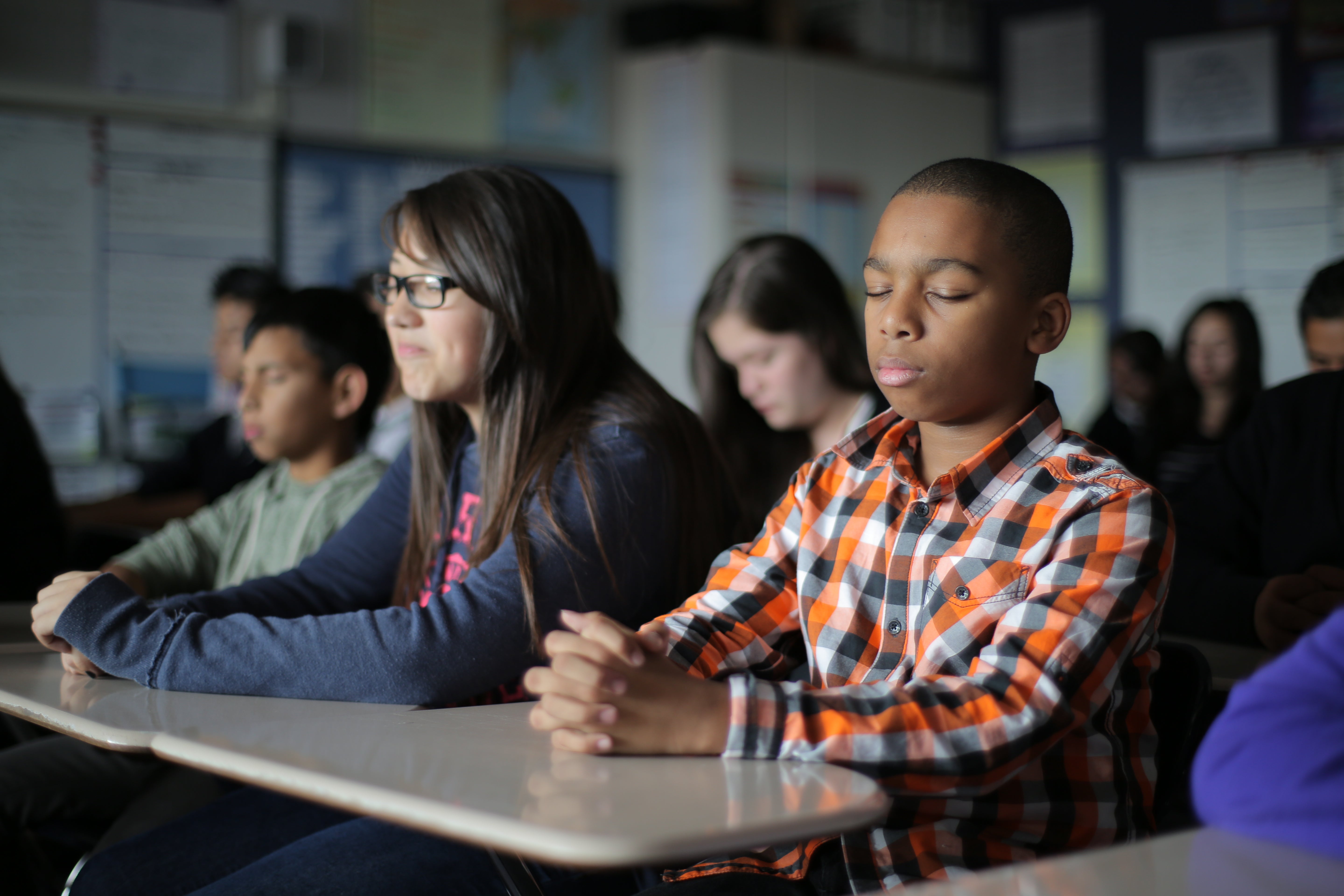 A group of children sit and meditate in a classroom