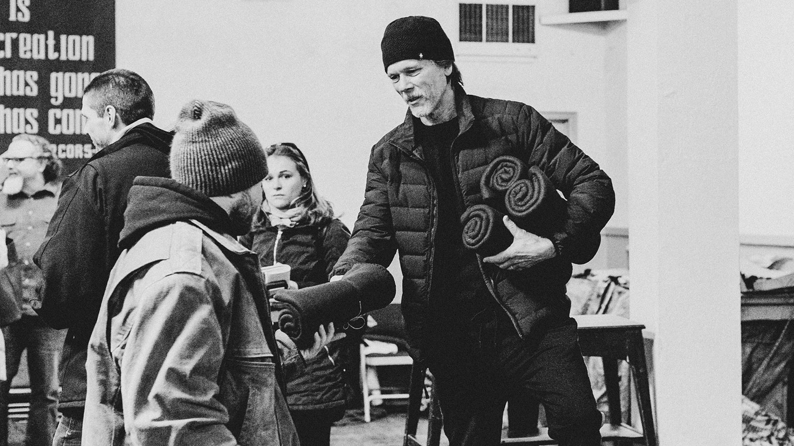 Kevin Bacon hands a blanket to a man.