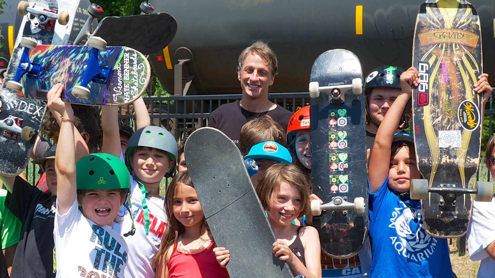 Tony Hawk is posing with a children and their skateboards.