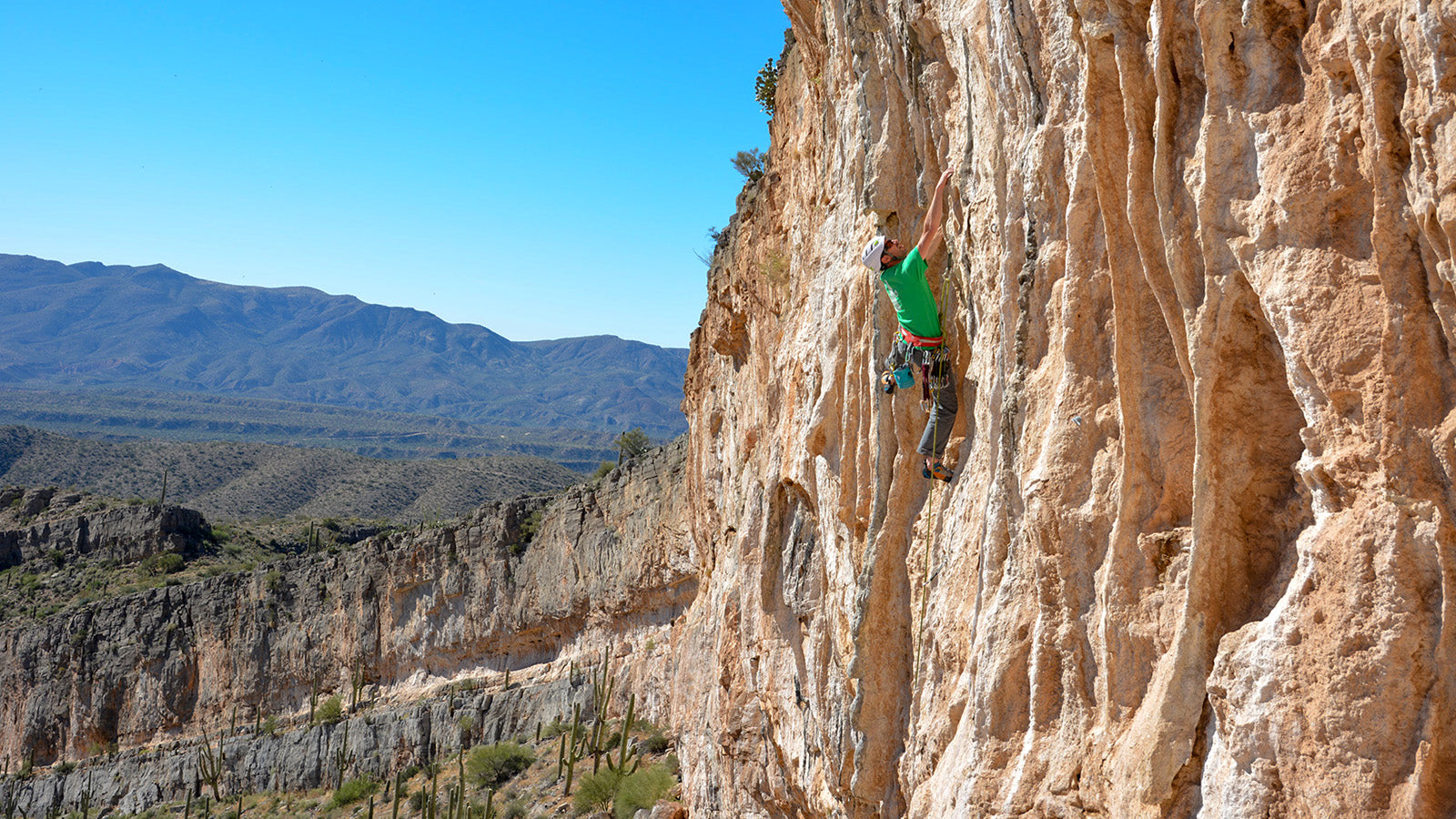 A rock climber half way up an orange cliff