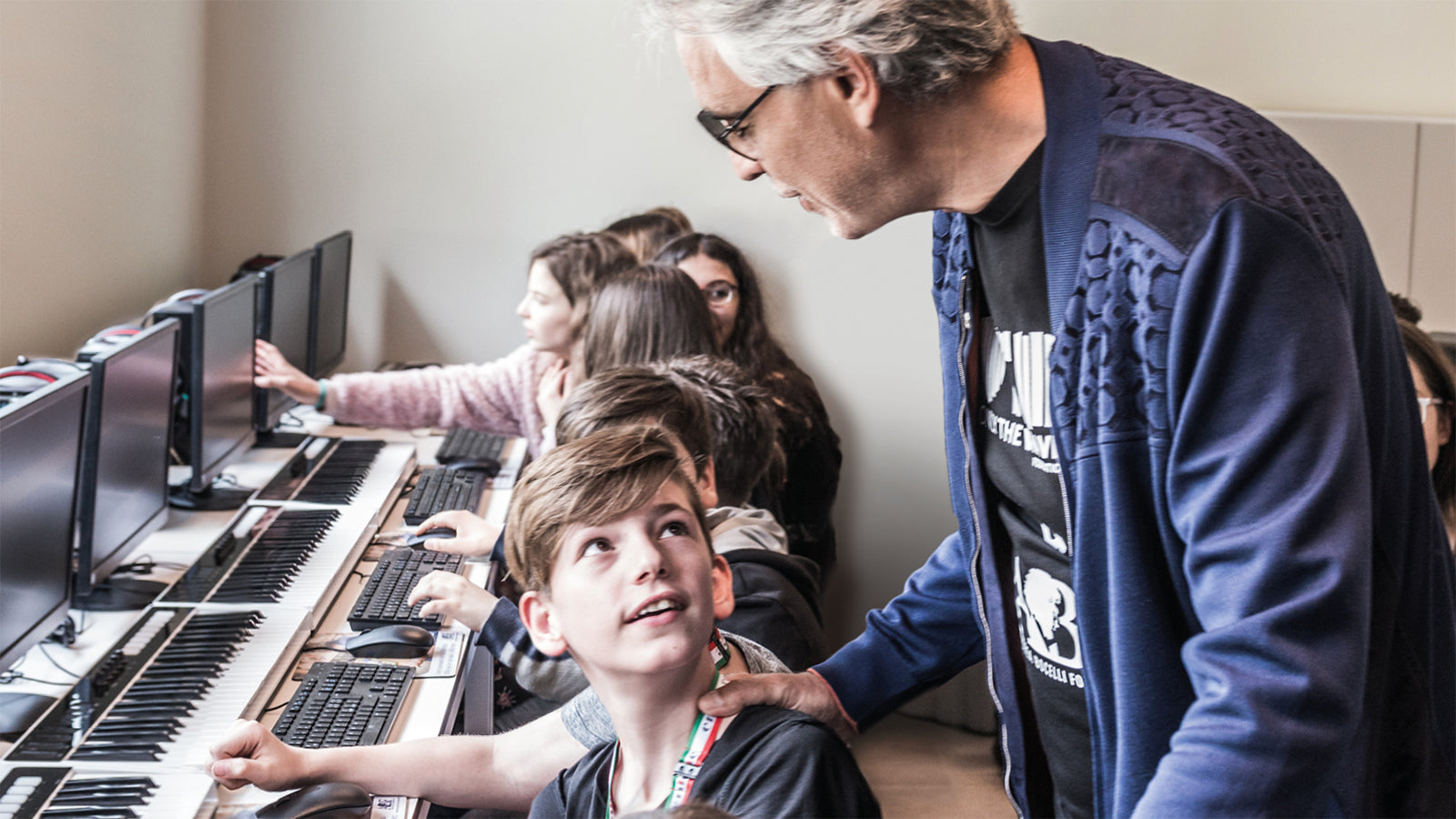 Andrea Bocelli speaking to a young boy sitting in a computer lab.